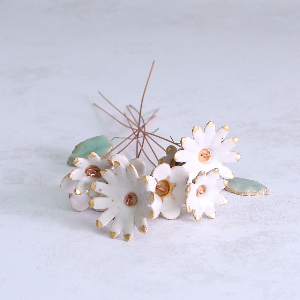 Handmade ceramic flower bouquet in white with gold-painted petals and copper wire stems displayed on a table