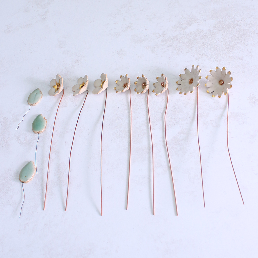 Handmade ceramic flower bouquet in white with gold-painted petals and copper wire stems laid out on a table.