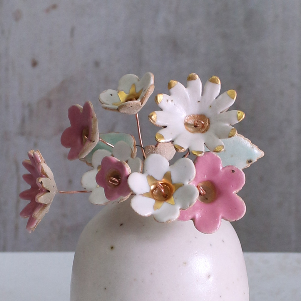 Handmade ceramic flower bouquet in white, pink, and fuchsia with gold-painted petals and copper wire stems displayed in a small ceramic vase.