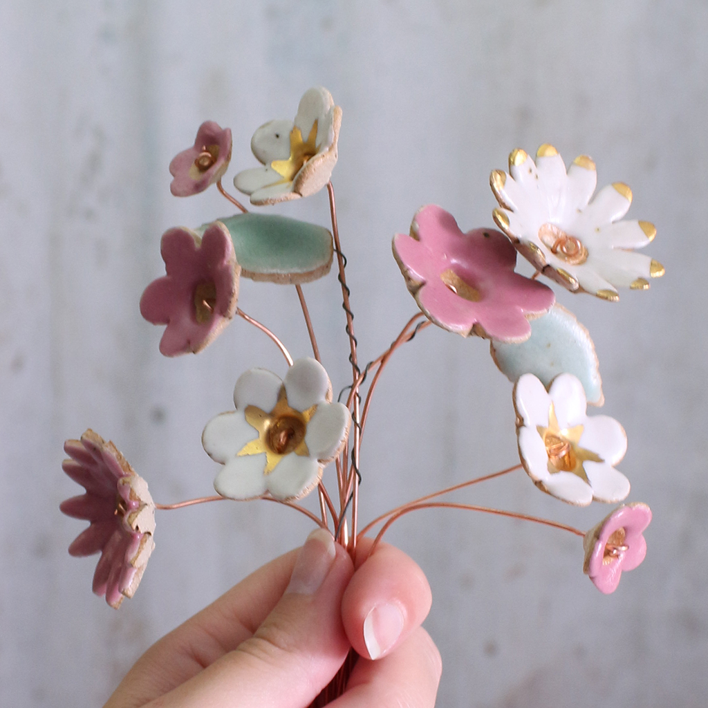 Handmade ceramic flower bouquet in white, pink, and fuchsia with gold-painted petals and copper wire stems being held.