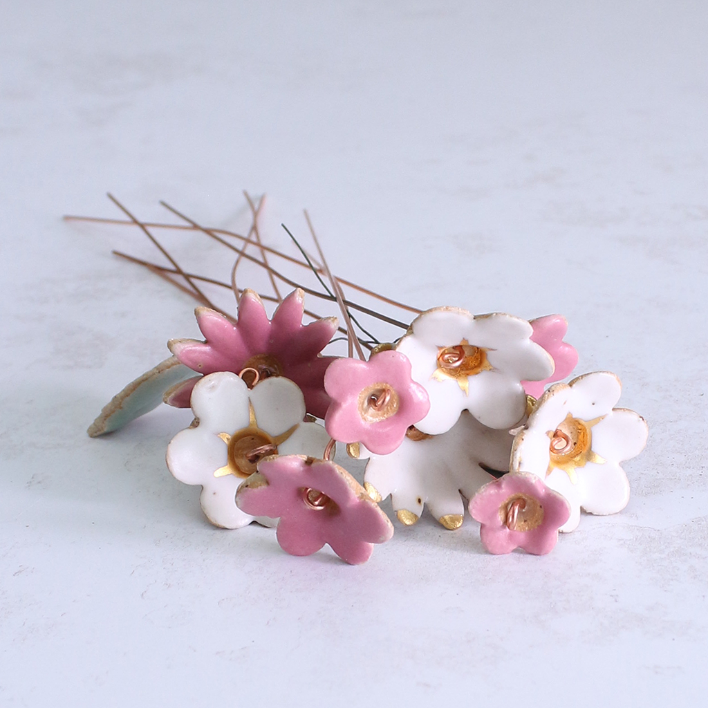Handmade ceramic flower bouquet in white, pink, and fuchsia with gold-painted petals and copper wire stems displayed on a table.