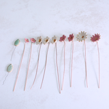 Handmade ceramic flower bouquet in white, pink, and fuchsia with gold-painted petals and copper wire stems displayed spread out on a table.