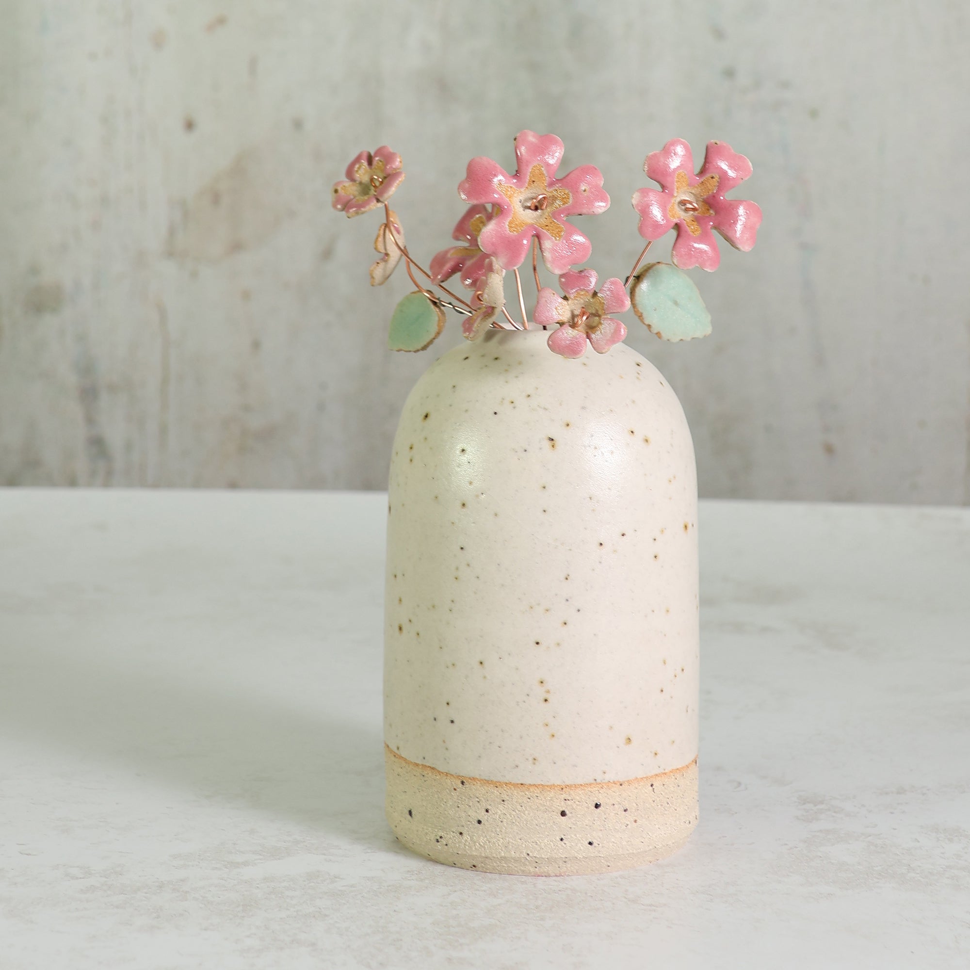 Speckled ceramic white vase with pink ceramic flowers on a light surface and textured background