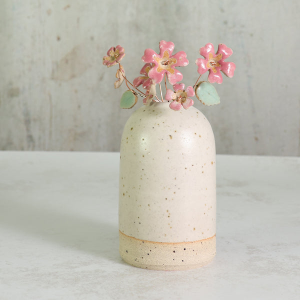 Speckled ceramic white vase with pink ceramic flowers on a light surface and textured background