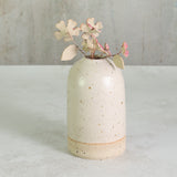 Ceramic vase with speckled texture holding ceramic flowers on a light background