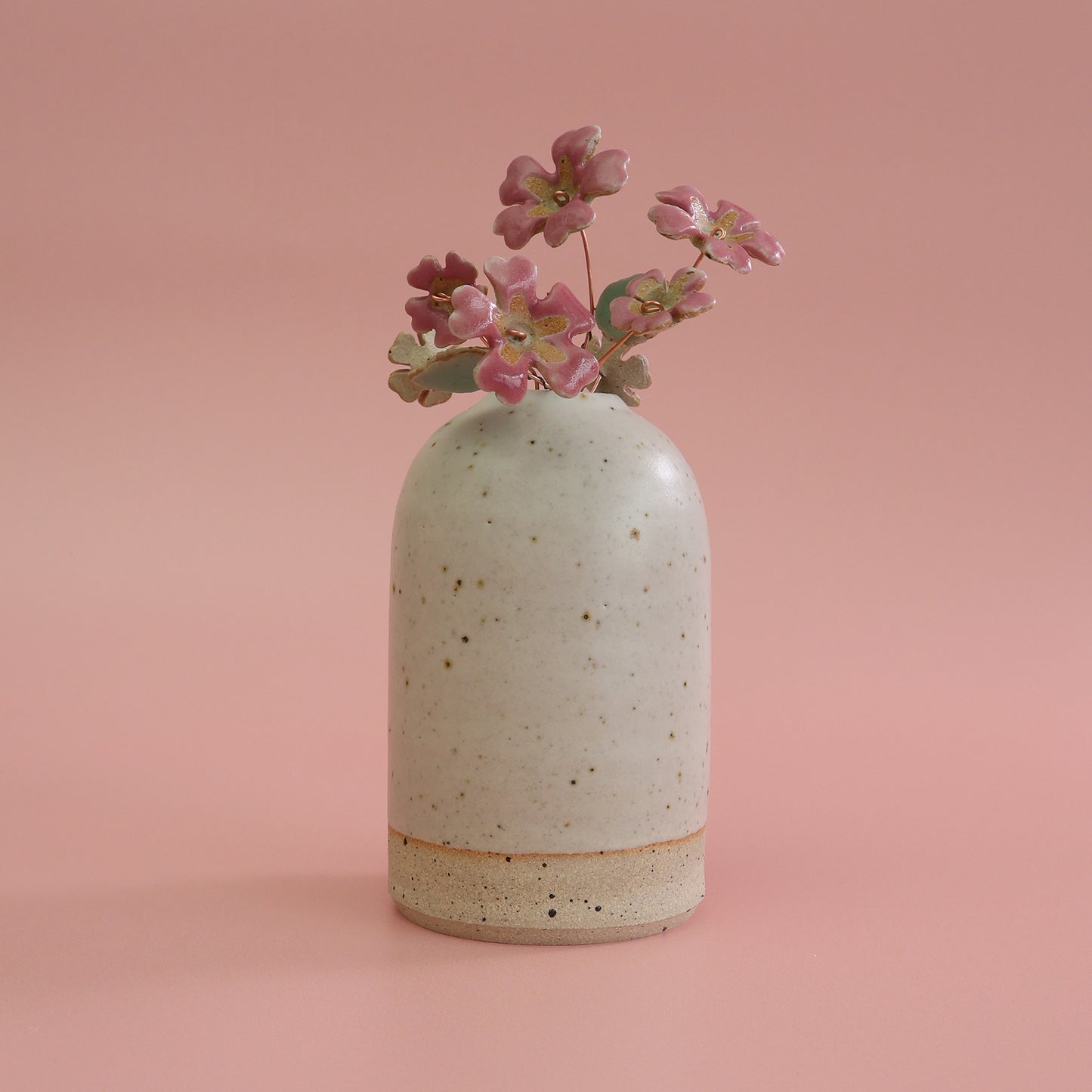 Speckled ceramic vase with pink primrose ceramic flowers on a pink background
