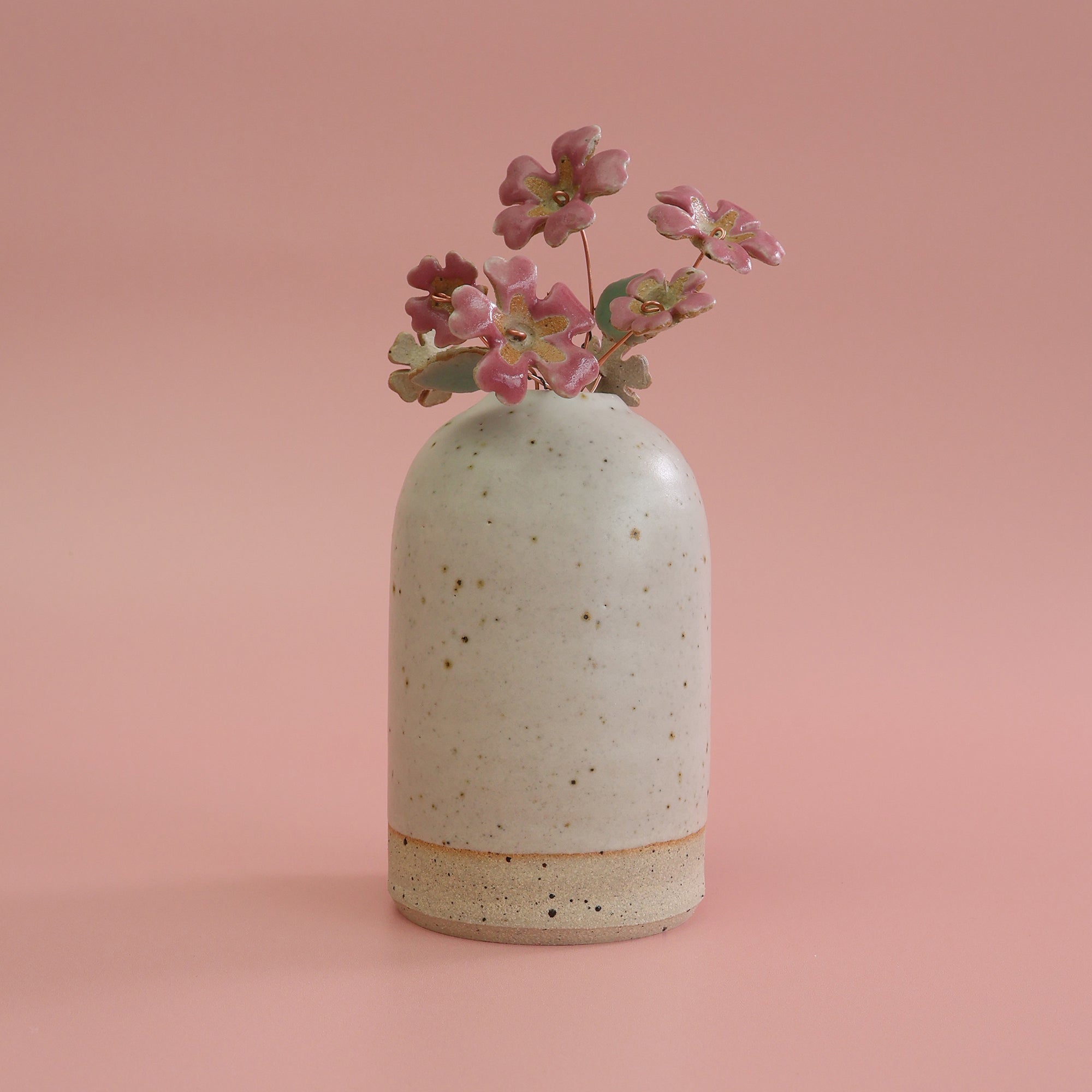 Speckled ceramic vase with pink primrose ceramic flowers on a pink background