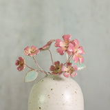 Small handmade white ceramic vase with pink ceramic primrose flowers on a light gray background