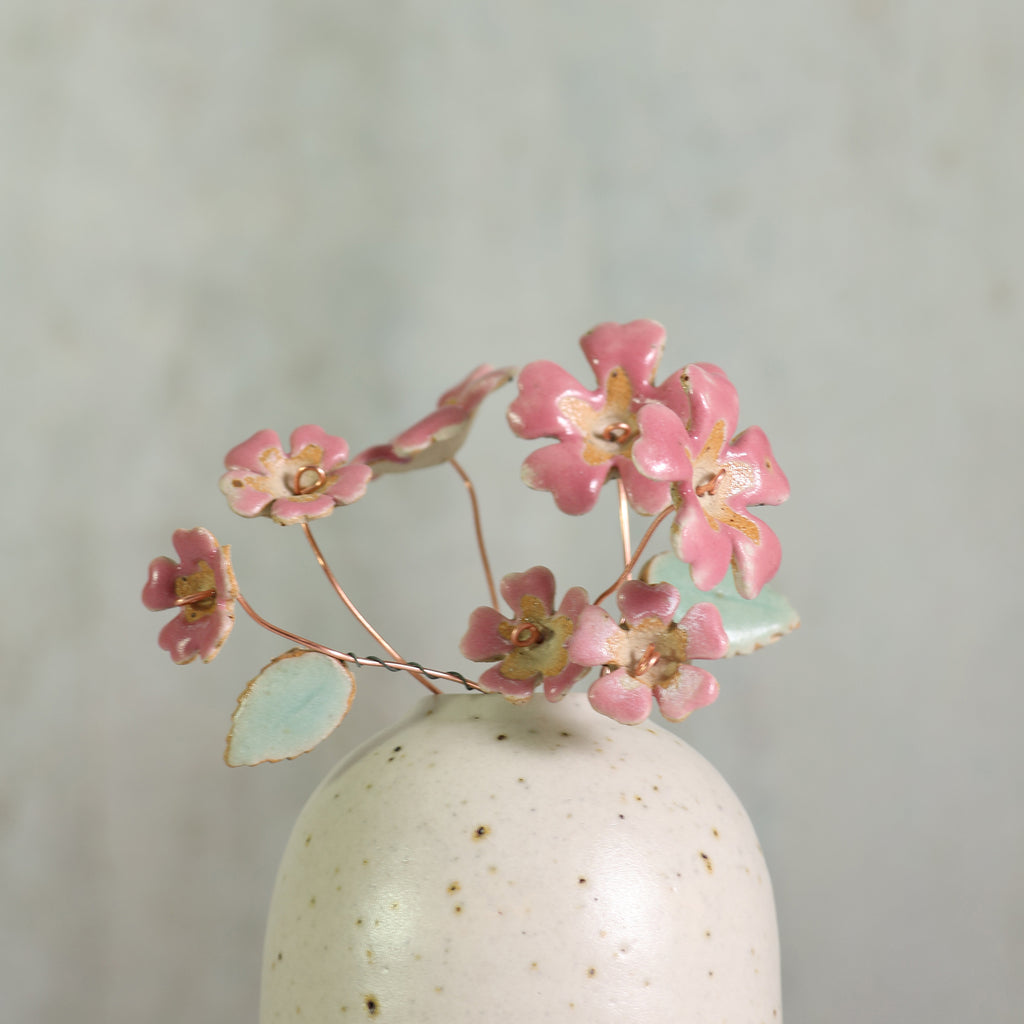 Small handmade white ceramic vase with pink ceramic primrose flowers on a light gray background