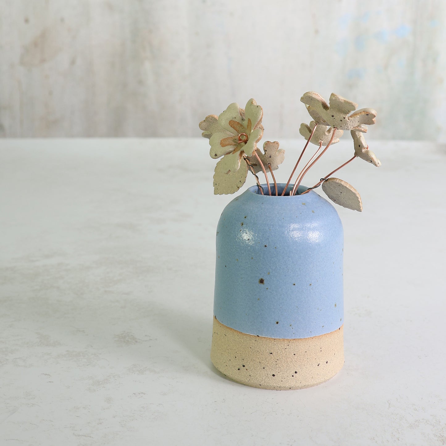 Ceramic vase with a blue top and beige bottom, containing ceramic flowers on a light background