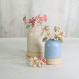 Two ceramic vases, one white and one blue, with handmade primrose flowers in pink and yellow on a light background