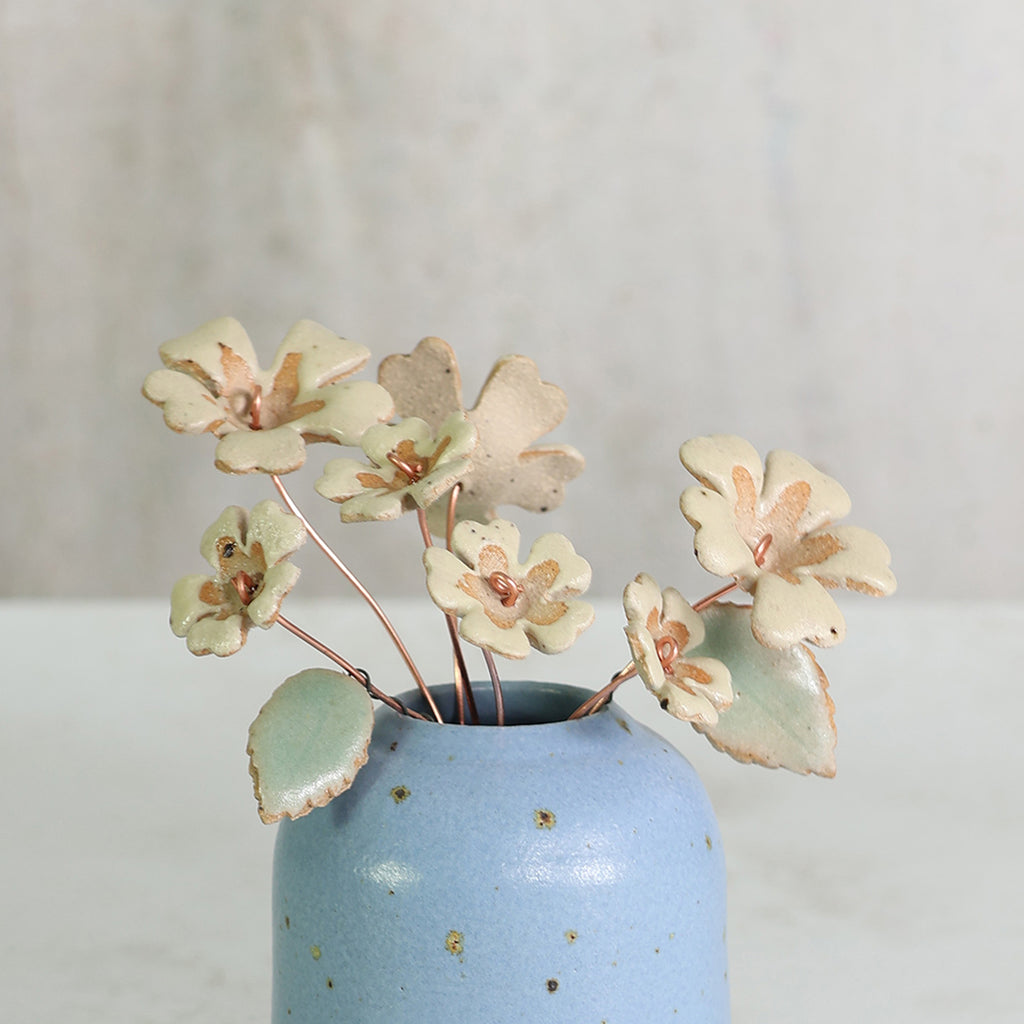 Small blue handmade ceramic vase with decorative ceramic primrose flowers on a neutral background