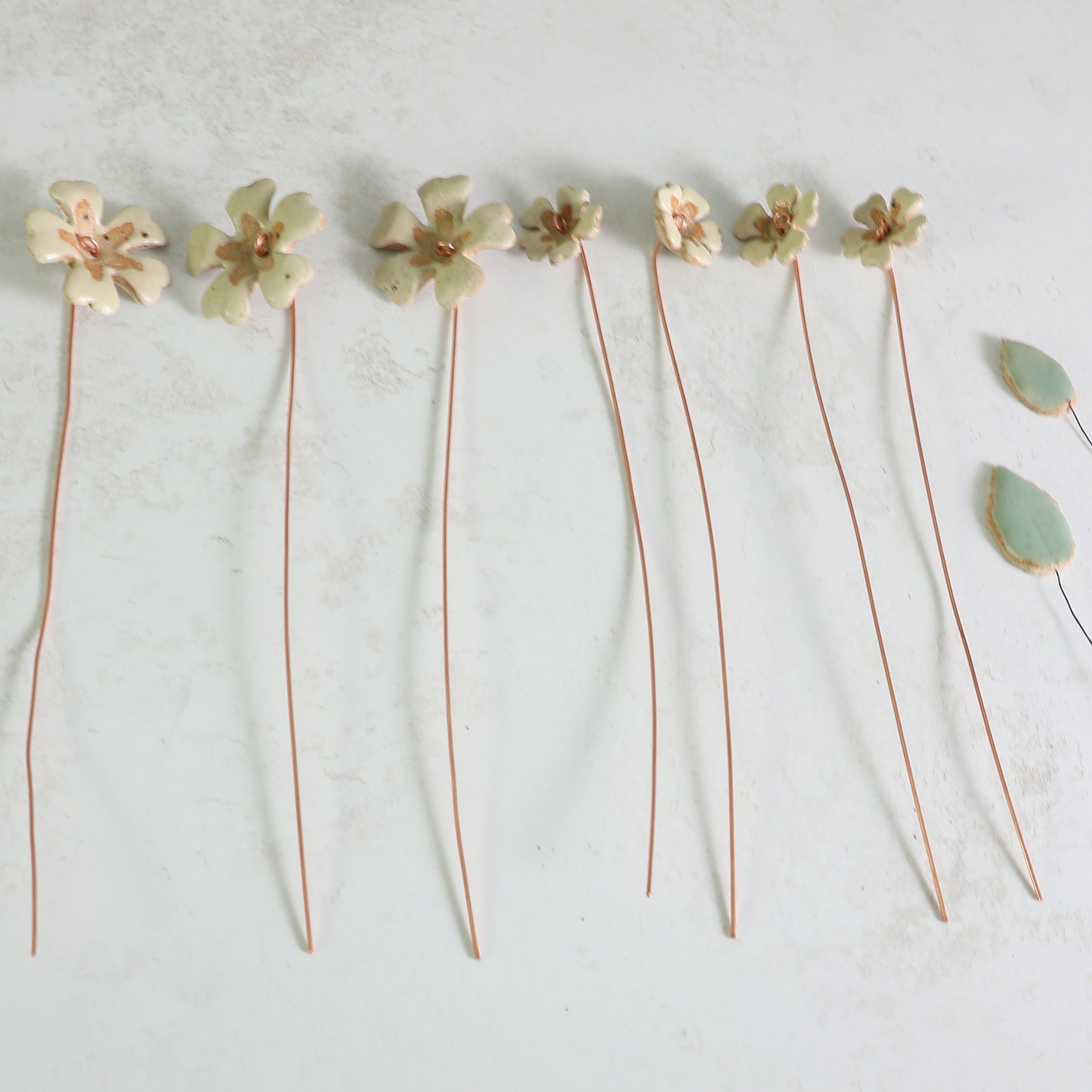 Ceramic primrose flowers on copper wire layed flat  on a light gray background