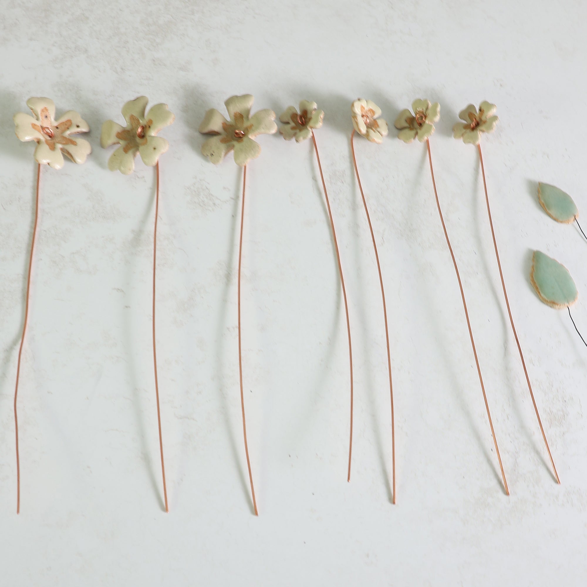 Ceramic primrose flowers on copper wire layed flat  on a light gray background