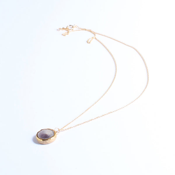 Gold necklace with a purple pendant on a white background