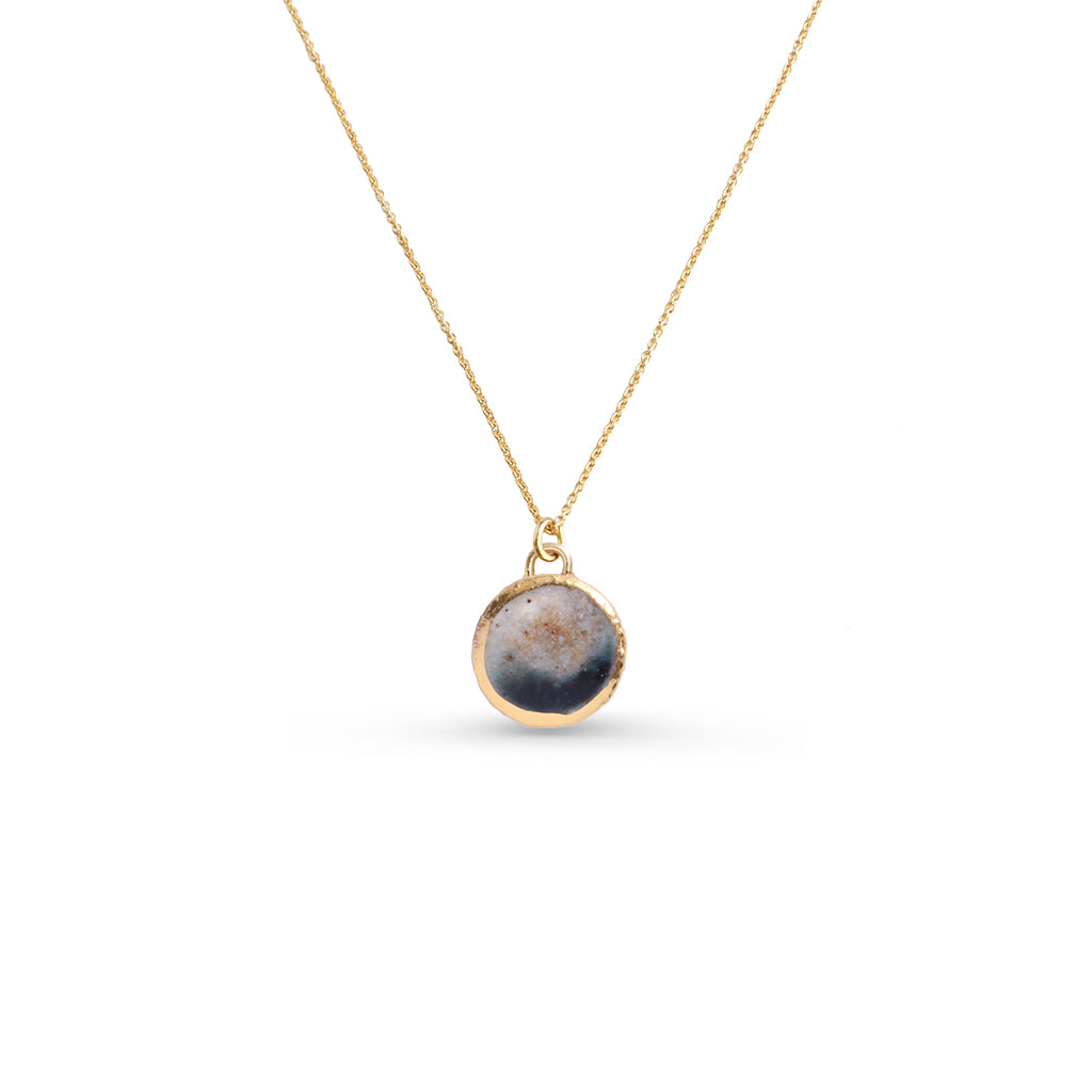 Gold necklace with a round earthy colour pendant on a white background