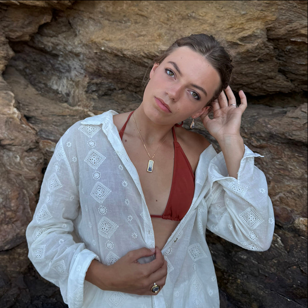 Woman in a red bikini top and white cover-up against a rocky background wearing handmade jewellery
