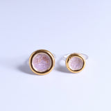 Two gold-rimmed rings with pink gemstones on a light grey background
