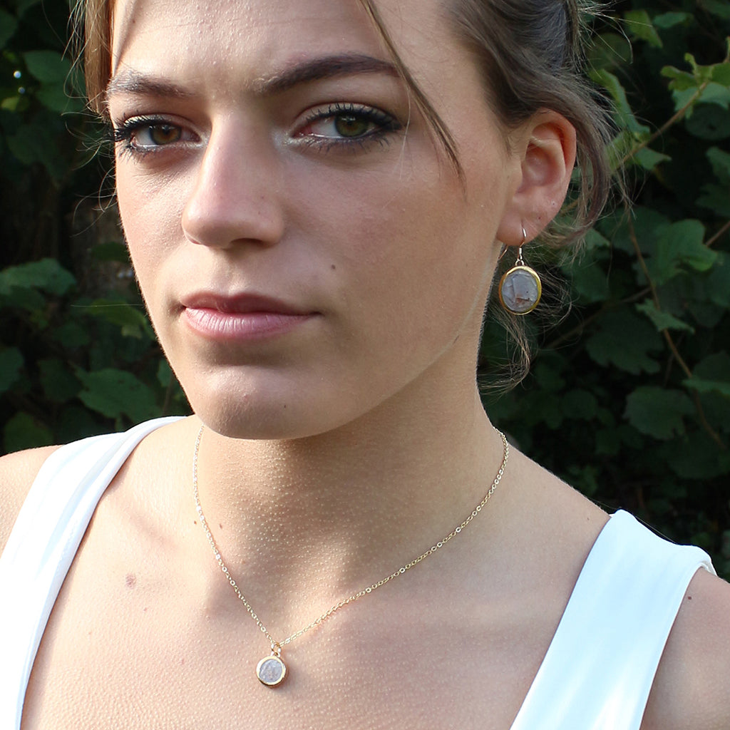 Woman wearing gold earrings and necklace with green foliage in the background