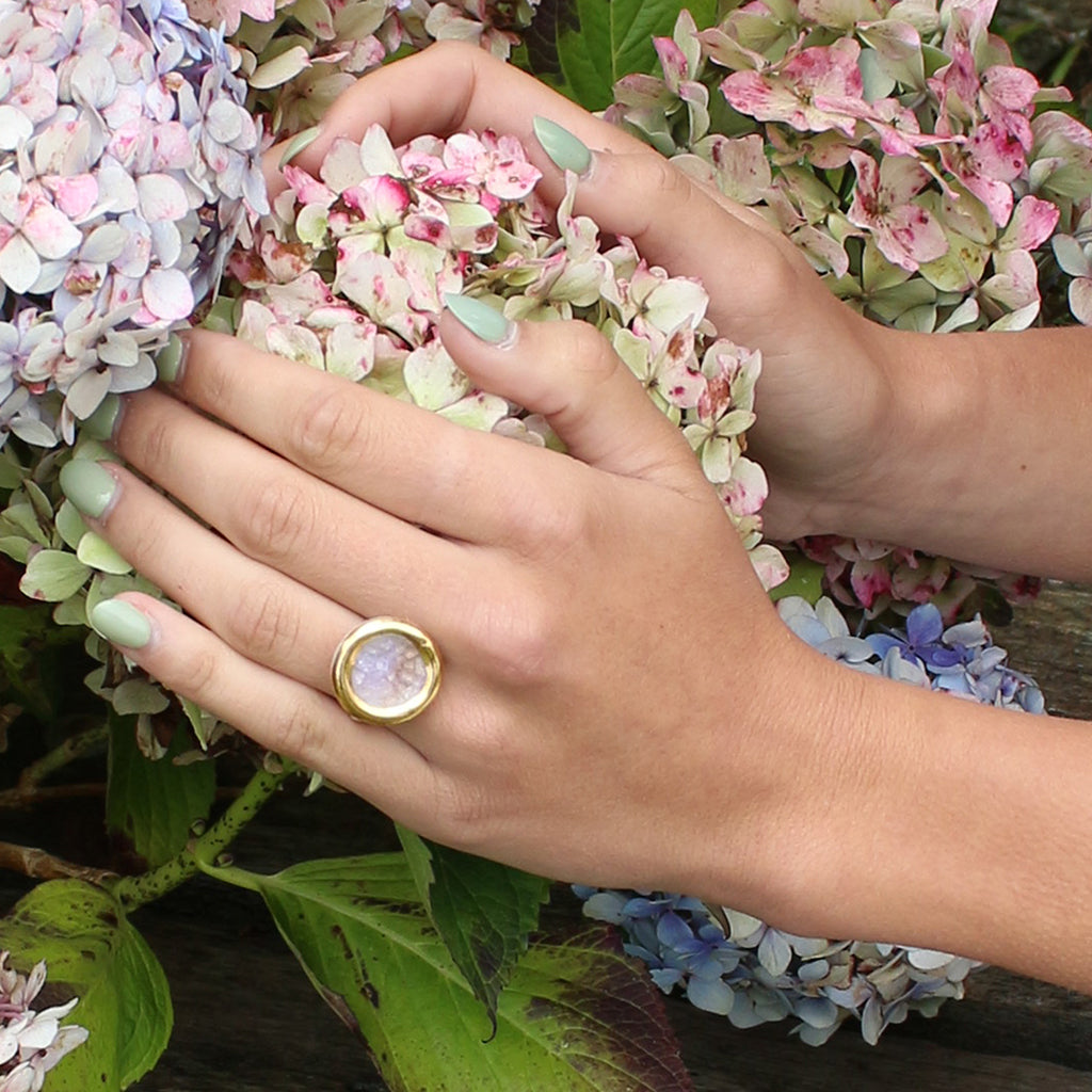 Hand wearing a gold ring with a pink stone, surrounded by hydrangea flowers