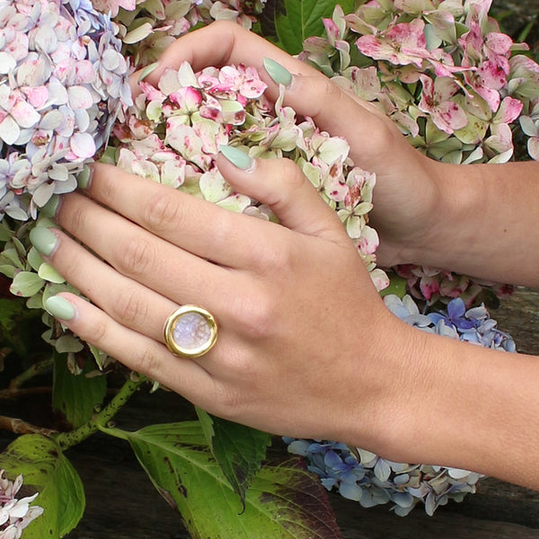Hand wearing a gold ring with a pink stone, surrounded by hydrangea flowers