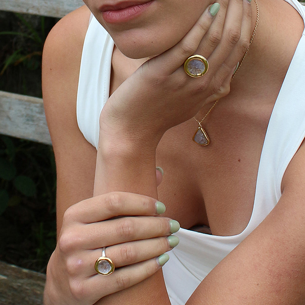 Close-up of a person wearing gold rings with pink elements on their fingers.