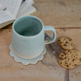 Mint green mug on flower coaster with cookies