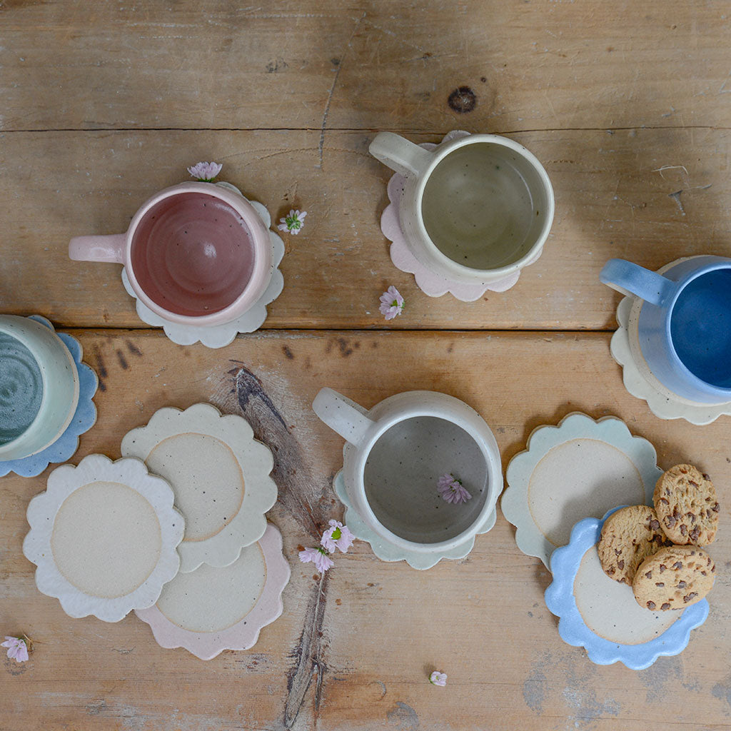 Handmade ceramic mugs and coasters on a wooden surface with cookies.