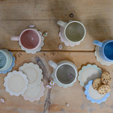 Handmade ceramic mugs and coasters on a wooden surface with cookies.