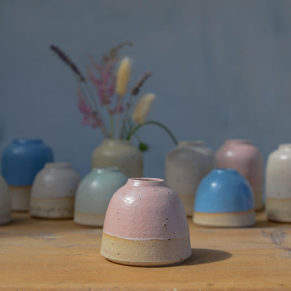 Close up of pink mini vase in sunlight in front of pastel vase collection