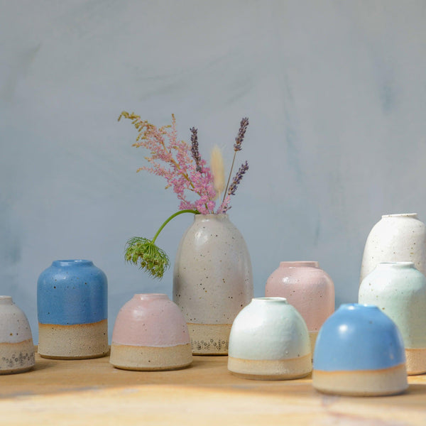 Medium white flower vase filled with wildflowers behind pastel vases