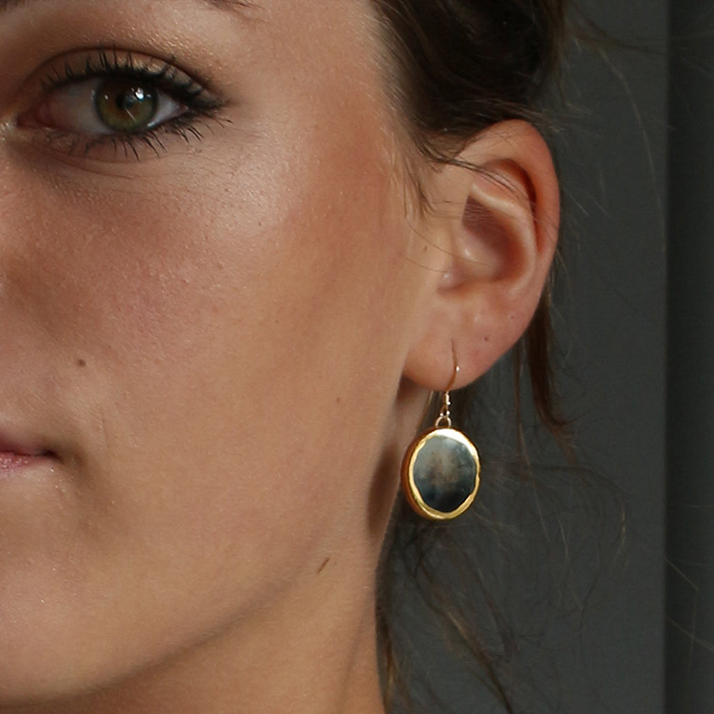 Close-up of a woman wearing a gold, blue and black earring.
