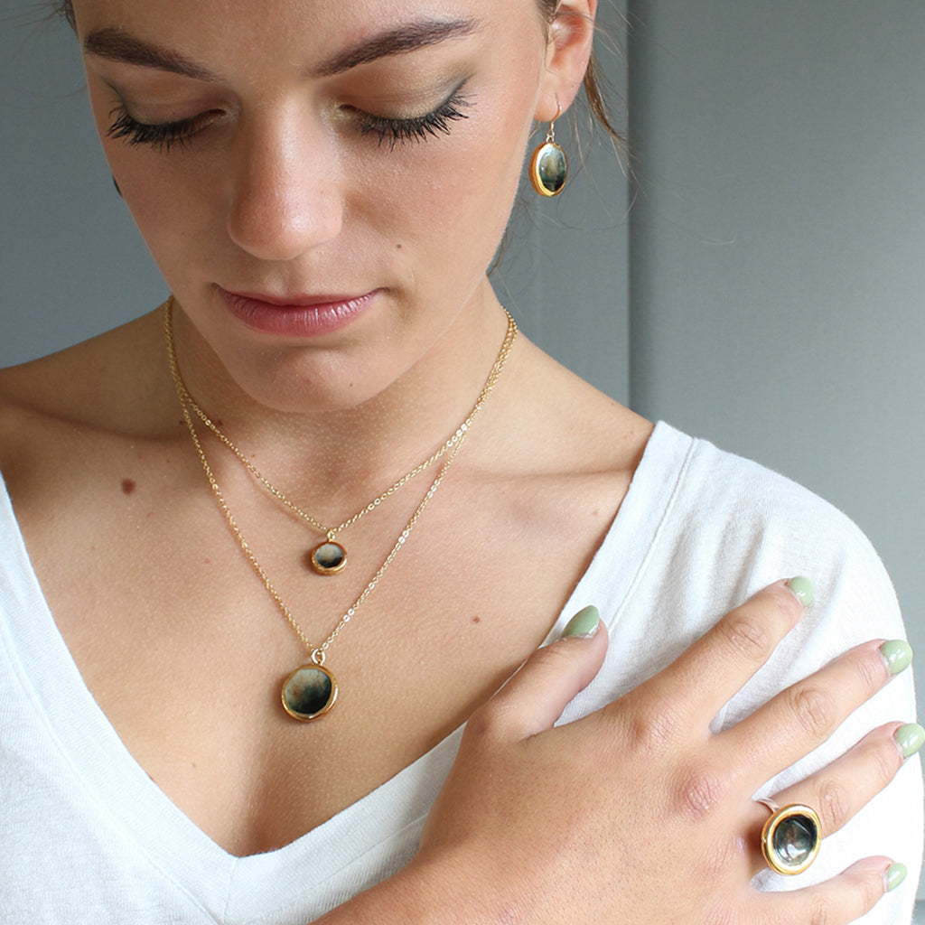 Woman wearing gold and black necklaces and earrings with a neutral background