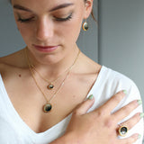 Woman wearing gold and black necklaces and earrings with a neutral background