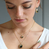 Woman wearing gold necklaces and earrings with a neutral background