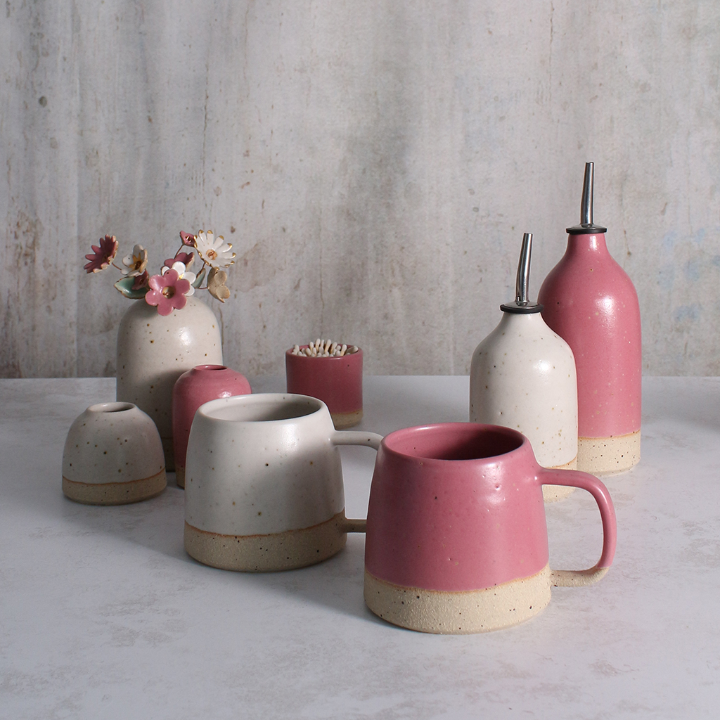 Collection of ceramic pots and mugs with pink and beige colors on a textured surface.