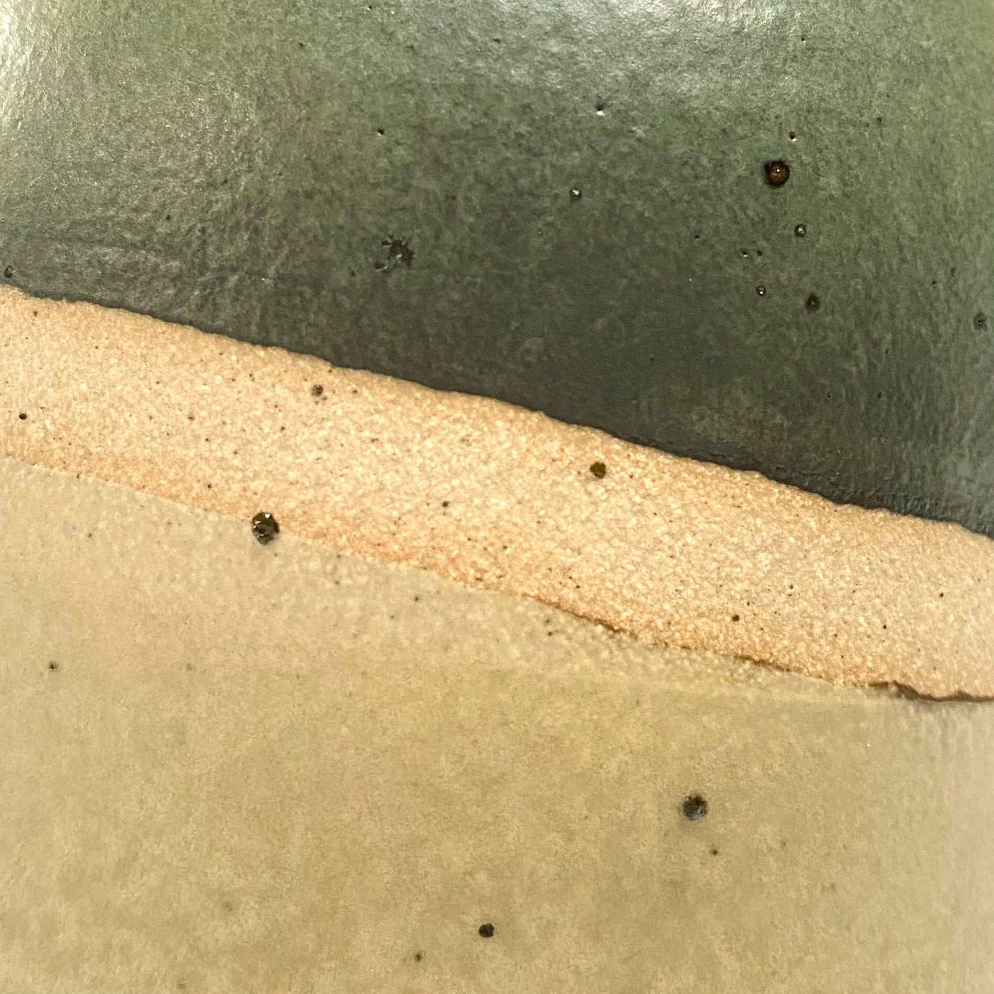 Close up green and light brown glazes against the exposed flecked clay