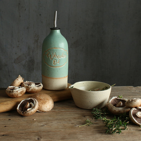 Mint green 'Wheeler Oil' example oil pourer on table setting surrounded by food