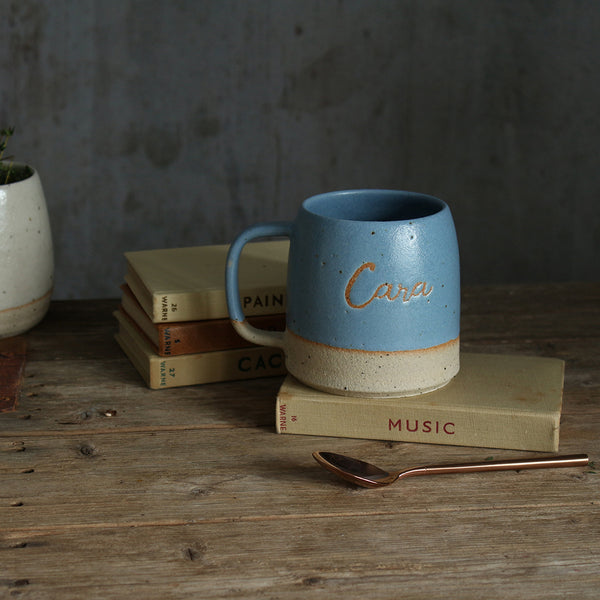 Blue 'Cara' stoneware mug resting on top of an old book