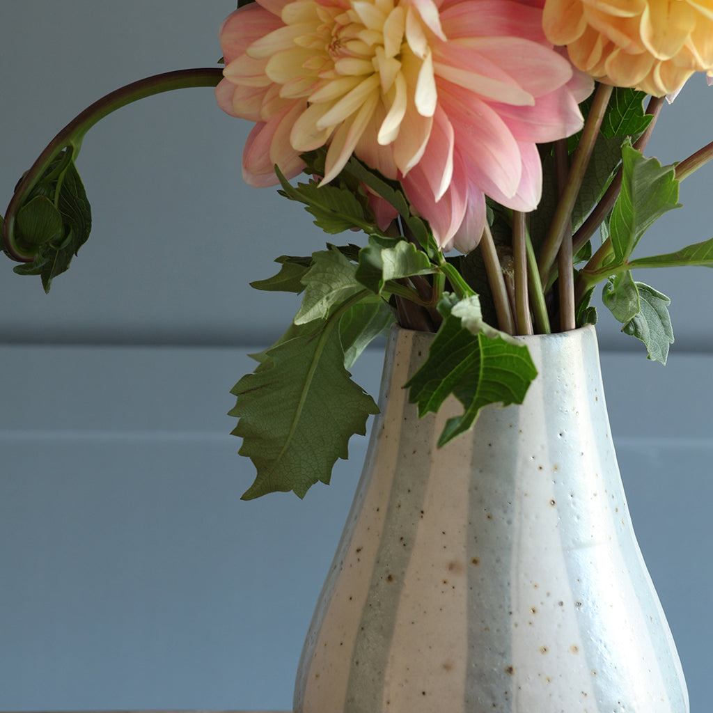A close-up of a ceramic vase filled with pink and yellow dahlia flowers and green leaves, set against a paneled background.