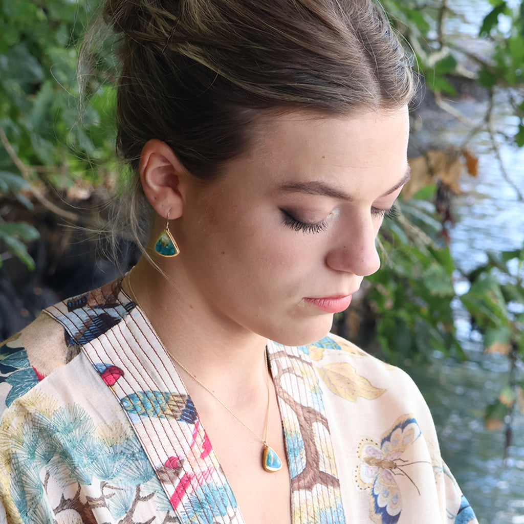 A women wearing a teardrop earring made from ceramic and teal glass with gold detailing, with a matching teardrop necklace. 