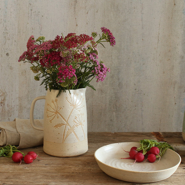 White pasta bowl with radishes in next to white pattered jug of wildflowers