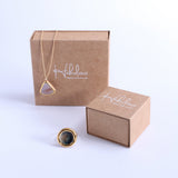 Cardboard jewellery packaging with Habulous branding pictured against a white background. Our Dusk Teardrop necklace with a gold chain and ceramic, glass and gold lustre pendant hangs over the box, and our large Eclipse Ring sits in the foreground. 