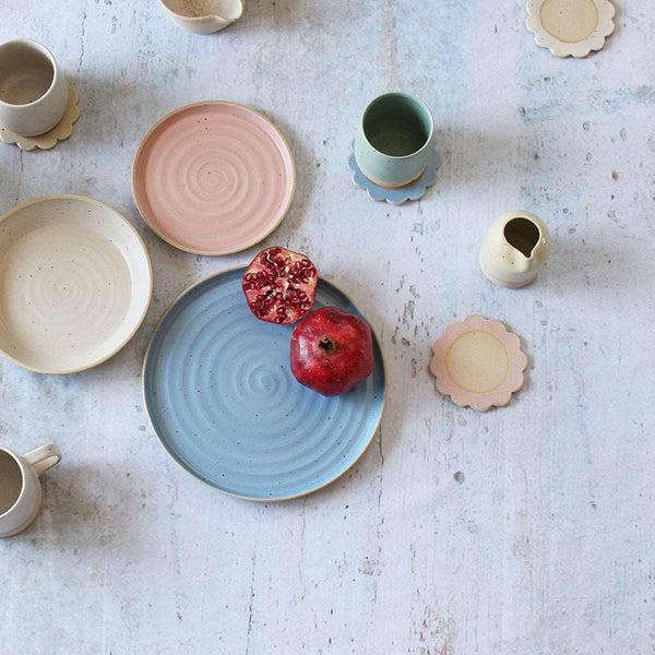 Spread of pastel plates, bowls, copasters, tumblers with sliced pomegranate