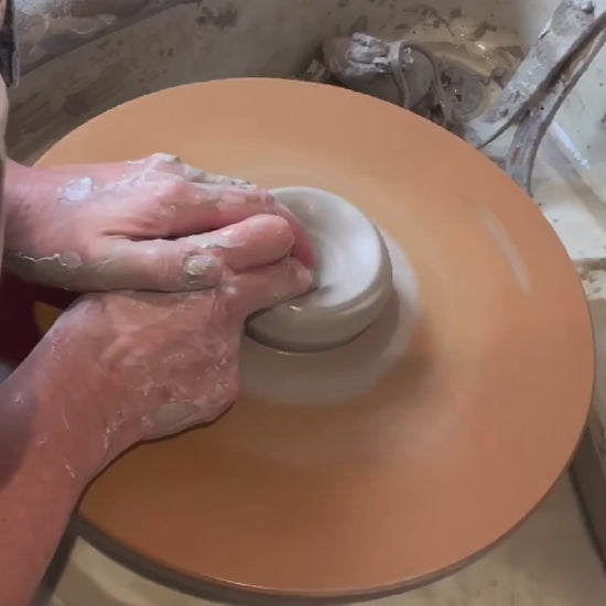 making a stoneware mug on a potters wheel, adding a handle and glazine to expose a wax resist flower design.