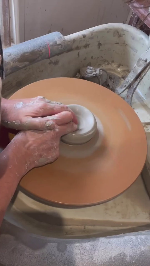 making a stoneware mug on a potters wheel, adding a handle and glazine to expose a wax resist flower design.