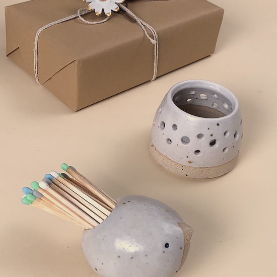 Video showing a ceramic bird matchpot which contains matches with a striking pad on the bottom of the bird. One of the matches is lit on the pad and used to light a tealight in a ceramic tealight holder. 
