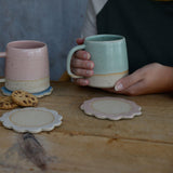 Mint Green Mug being held next to pink mug and flower coasters on table