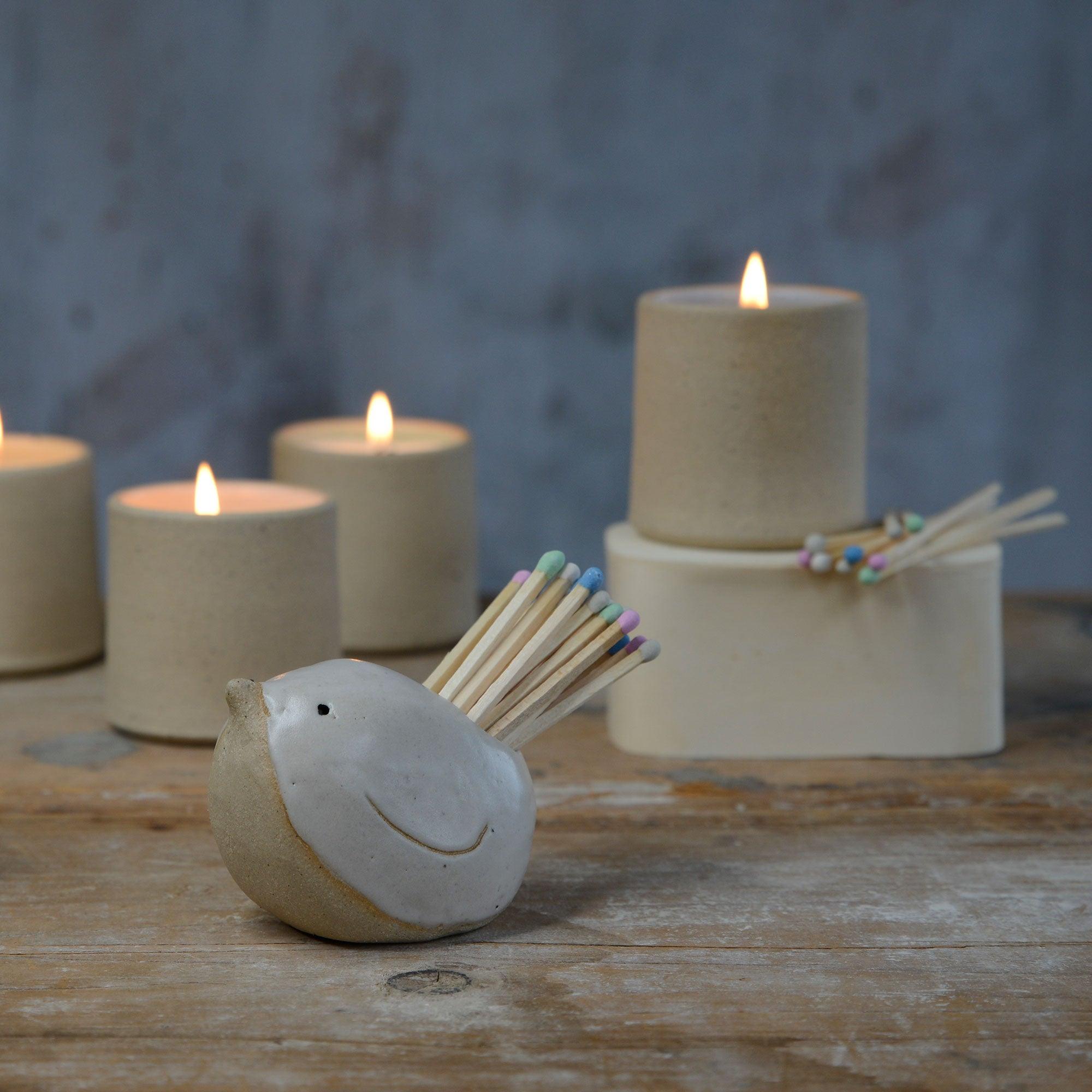 White bird with pastel matches in front of lit stoneware candles