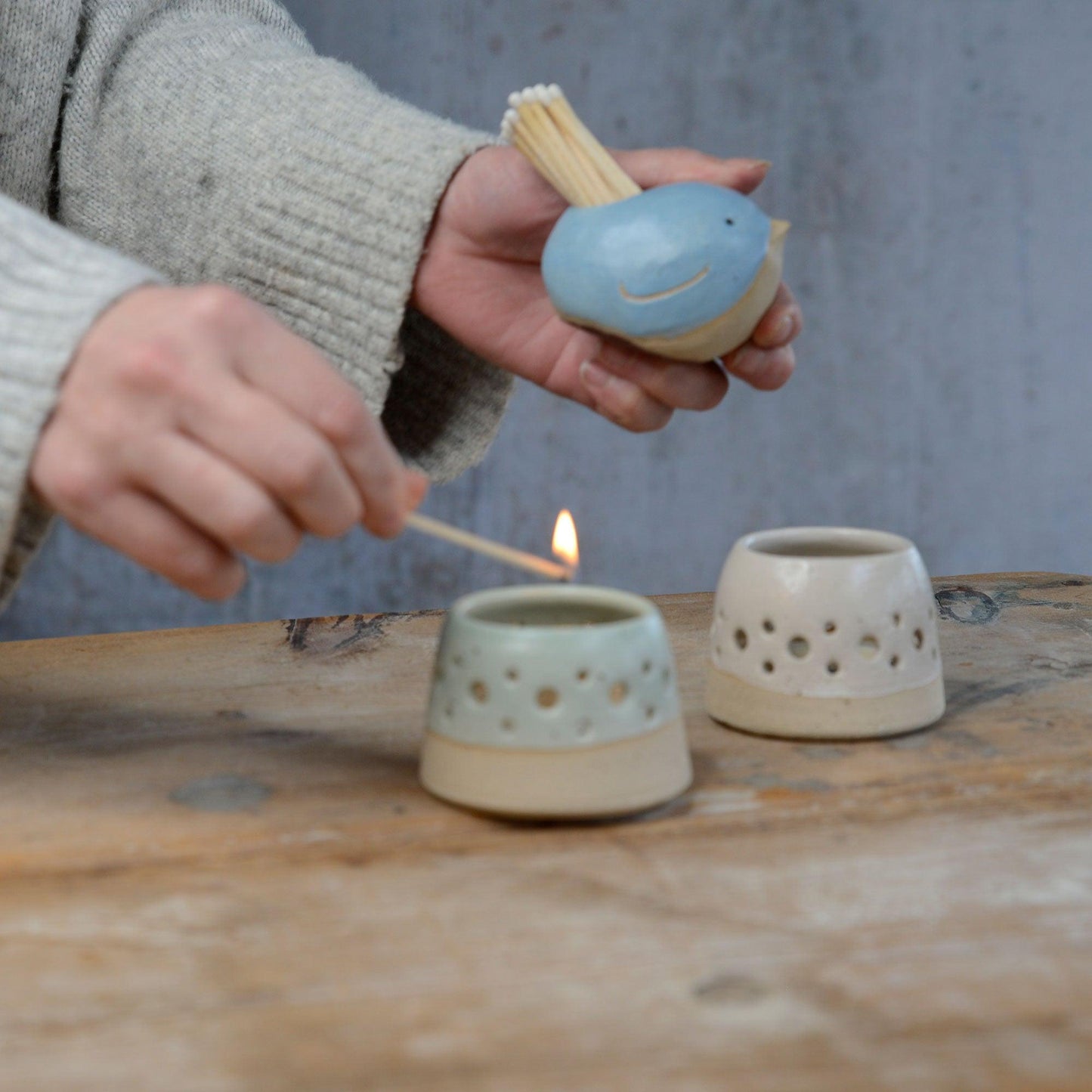 Bird match pot being held with match lighting tealight